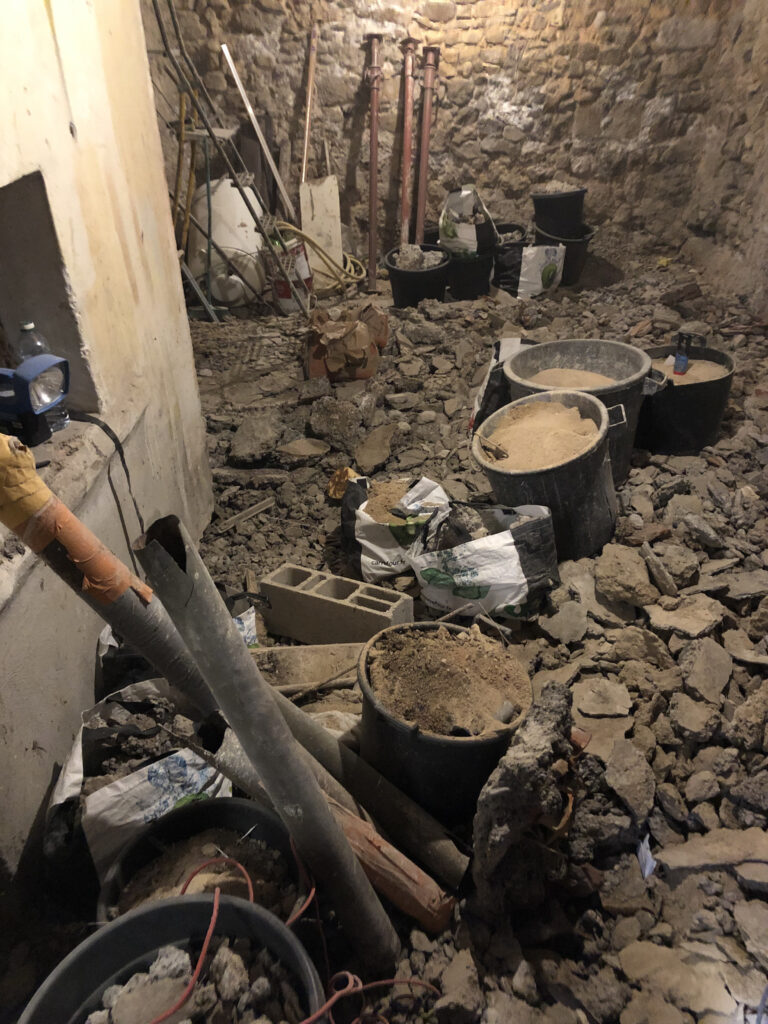 Cave à l’état brut avant rénovation, sol en gravats, étais métalliques et murs en pierre apparente non traités.