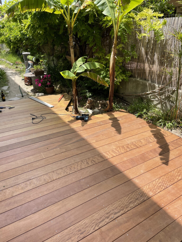 Terrasse en bois exotique terminée, lames alignées et vissées près des bananiers.