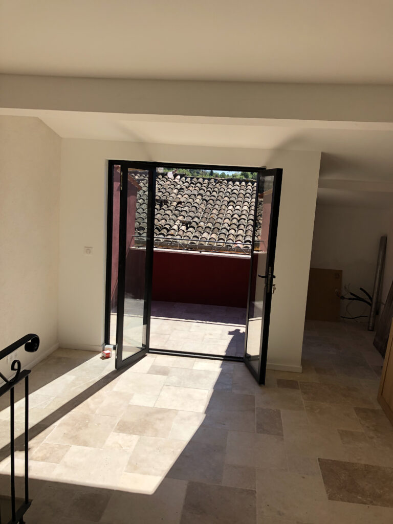 Percement en cours dans le mur donnant sur la future terrasse, gravats au sol, étai rouge et ouverture brute laissant voir les tuiles du voisinage.